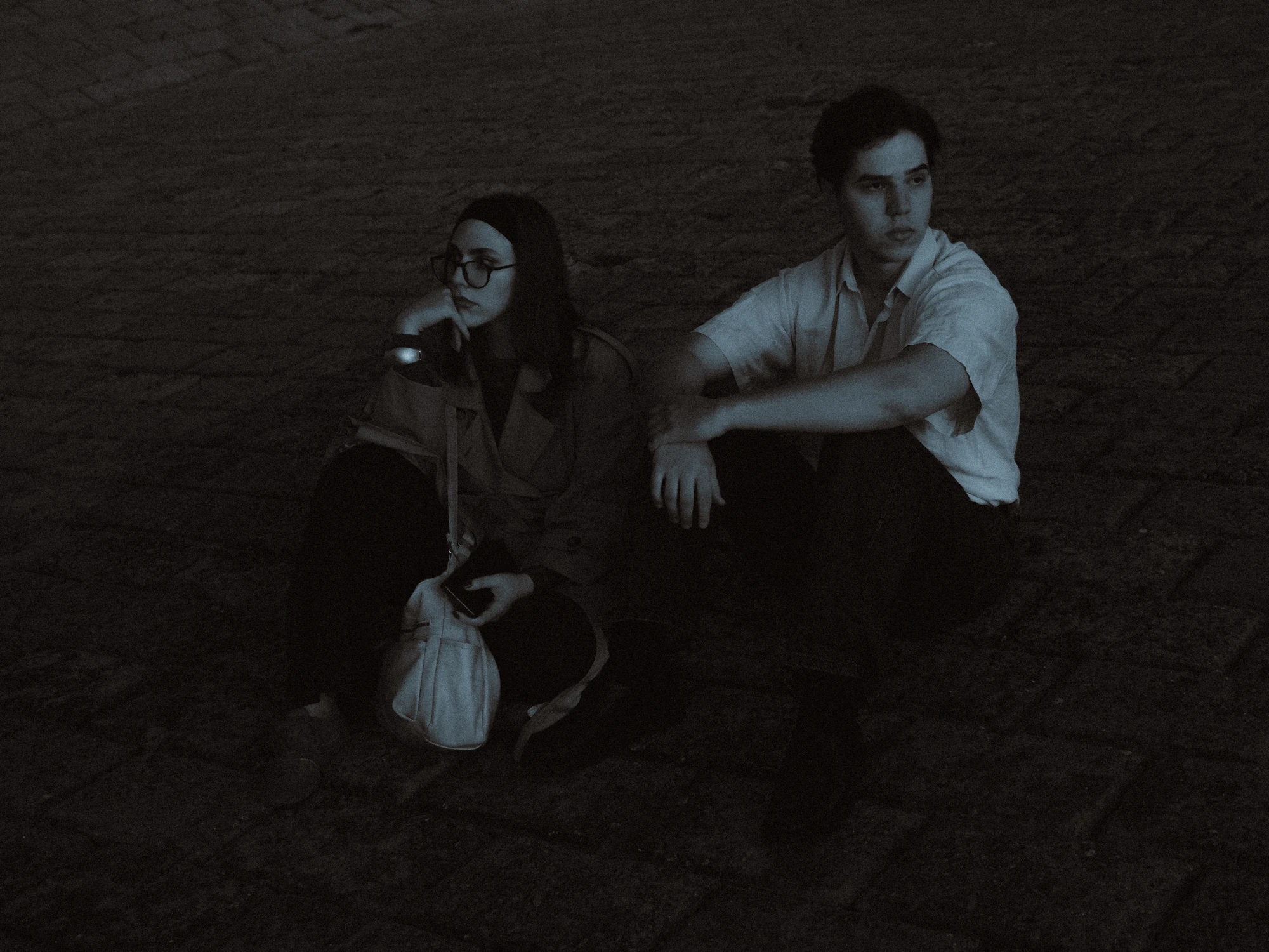 Young couple sitting on a cobblestone ground at dusk