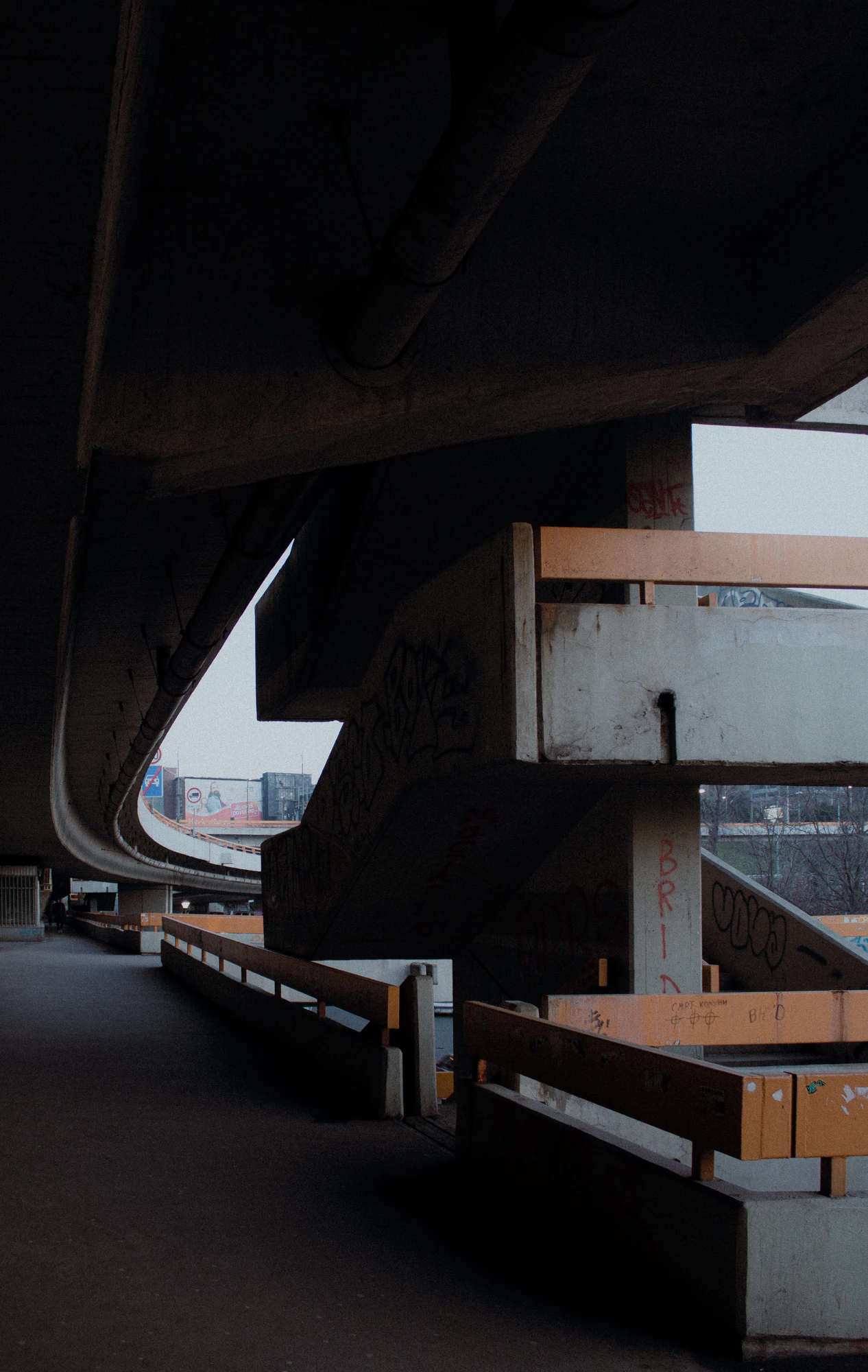 Curved roadway under a concrete overpass with safety barriers and geometric shadows