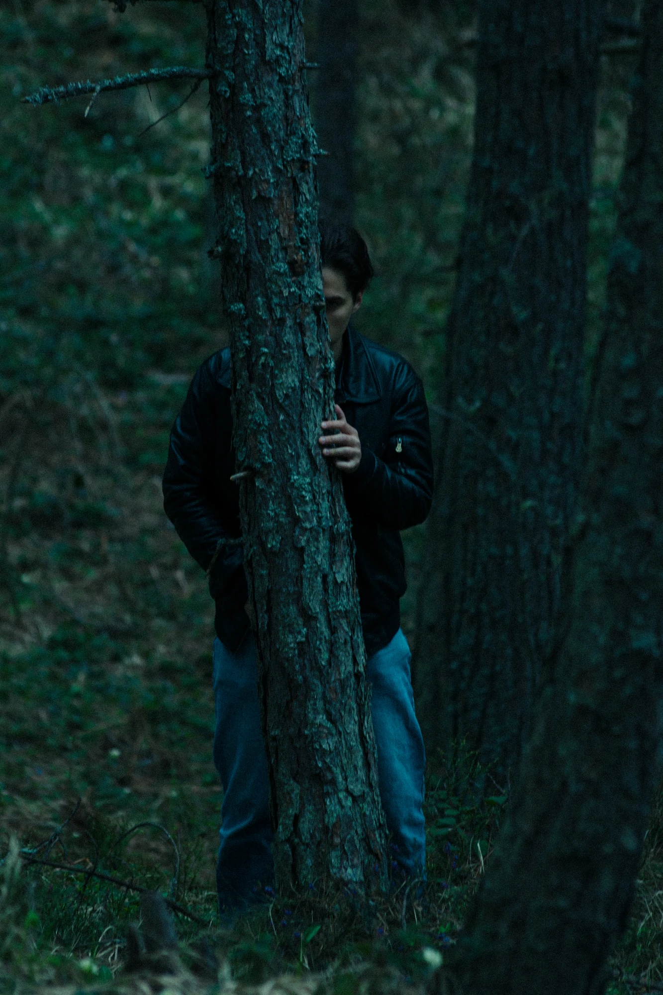 A man ominously standing behind a tree in the woods