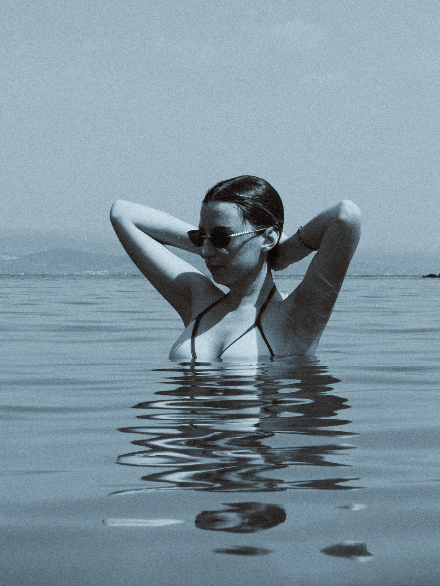 A woman standing in the sea, her reflection shuttered by the gentle waves