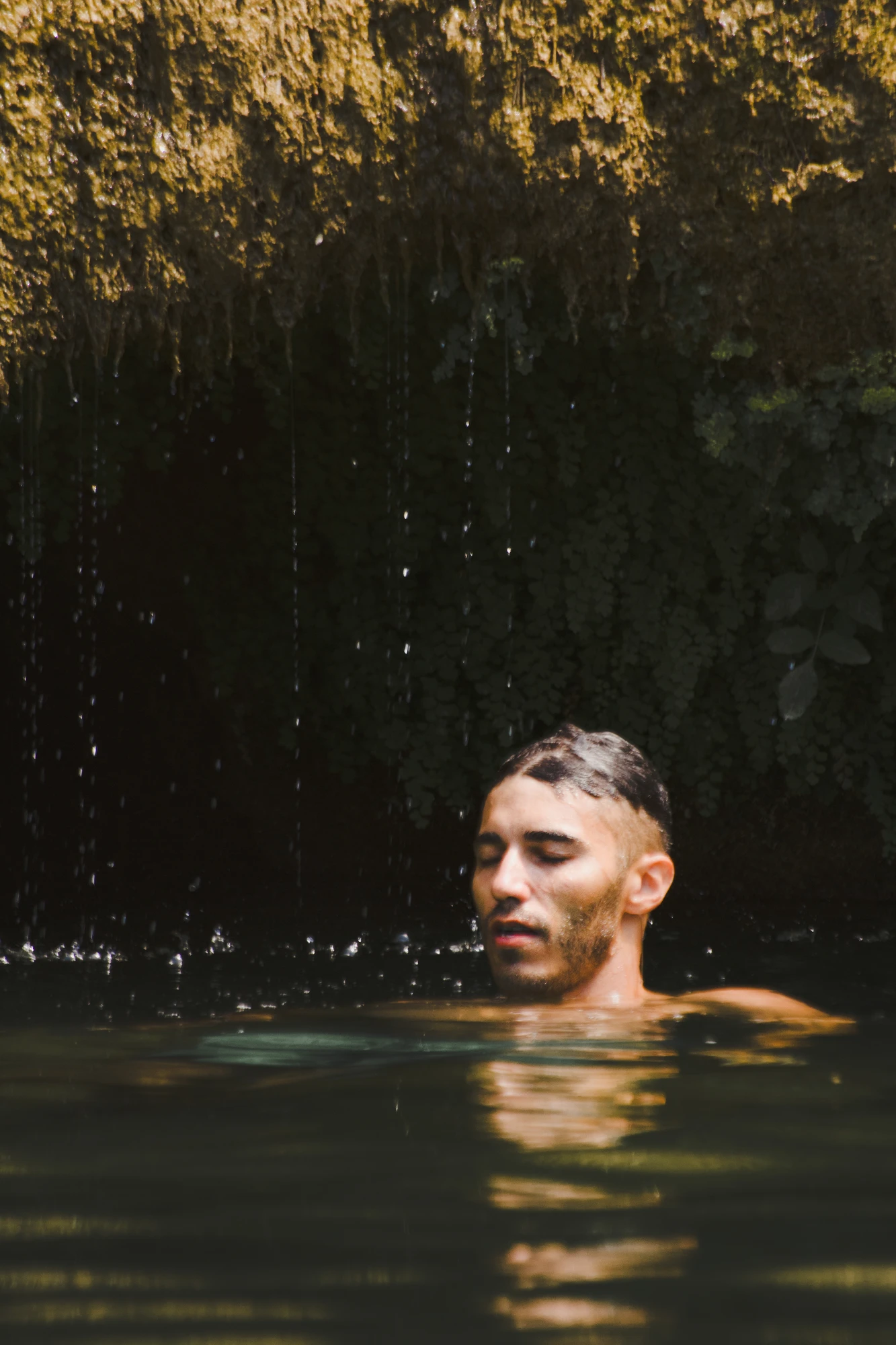 A person's head with closed eyes floating atop the water in front of a cave