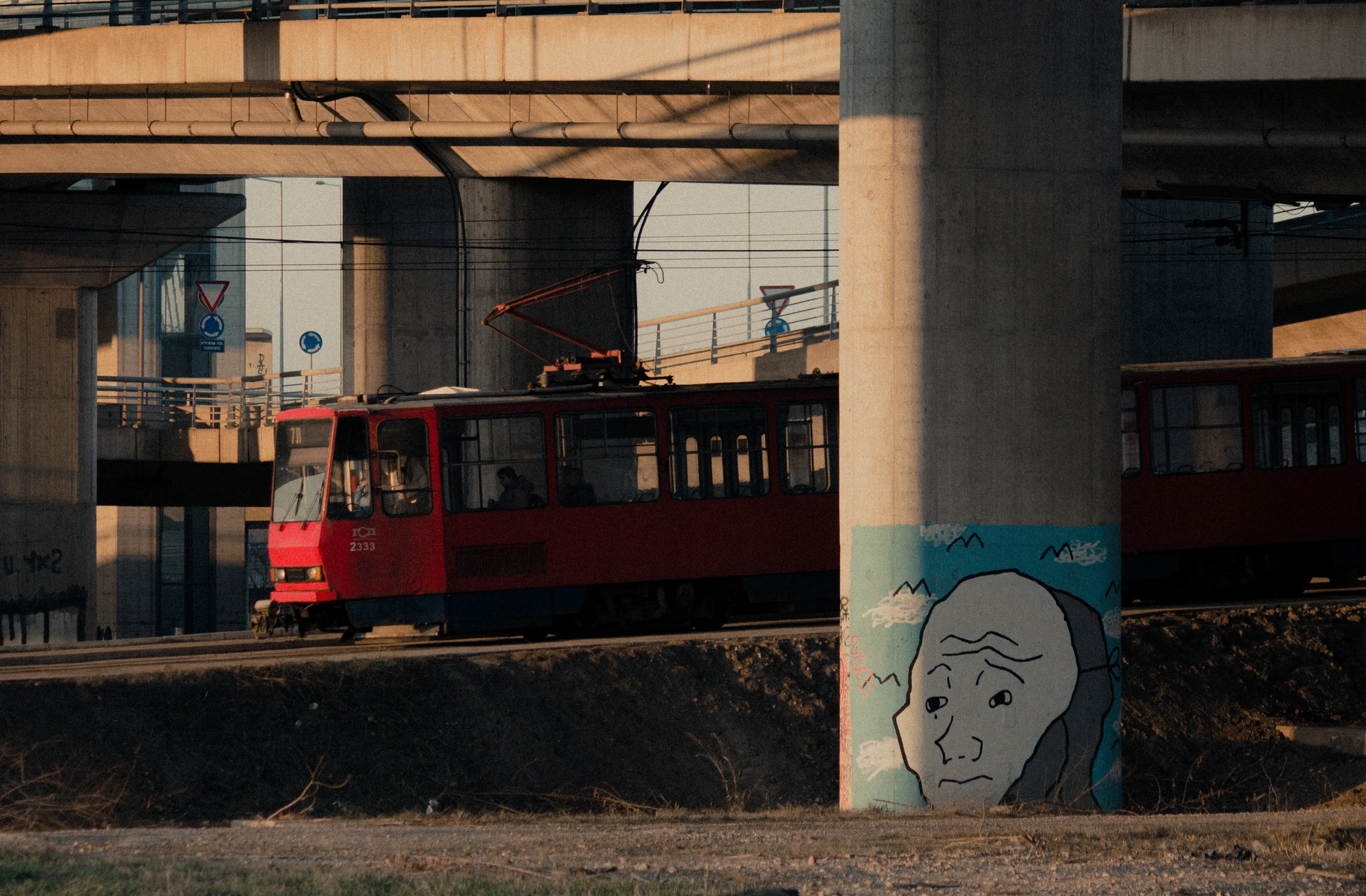 A red tram going through an underpass with wojak graffiti