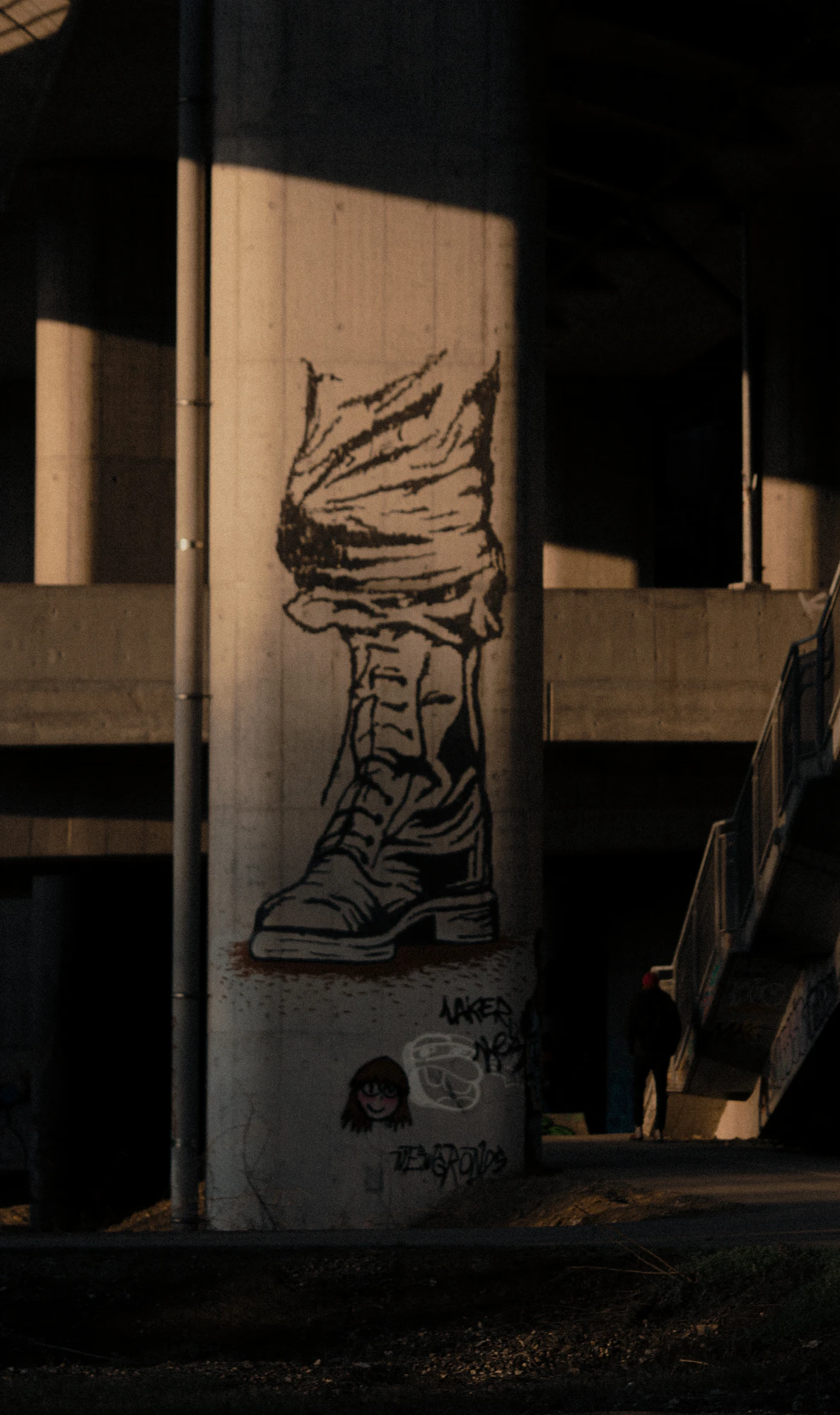 Graffiti art of a boots on a concrete pillar under a bridge