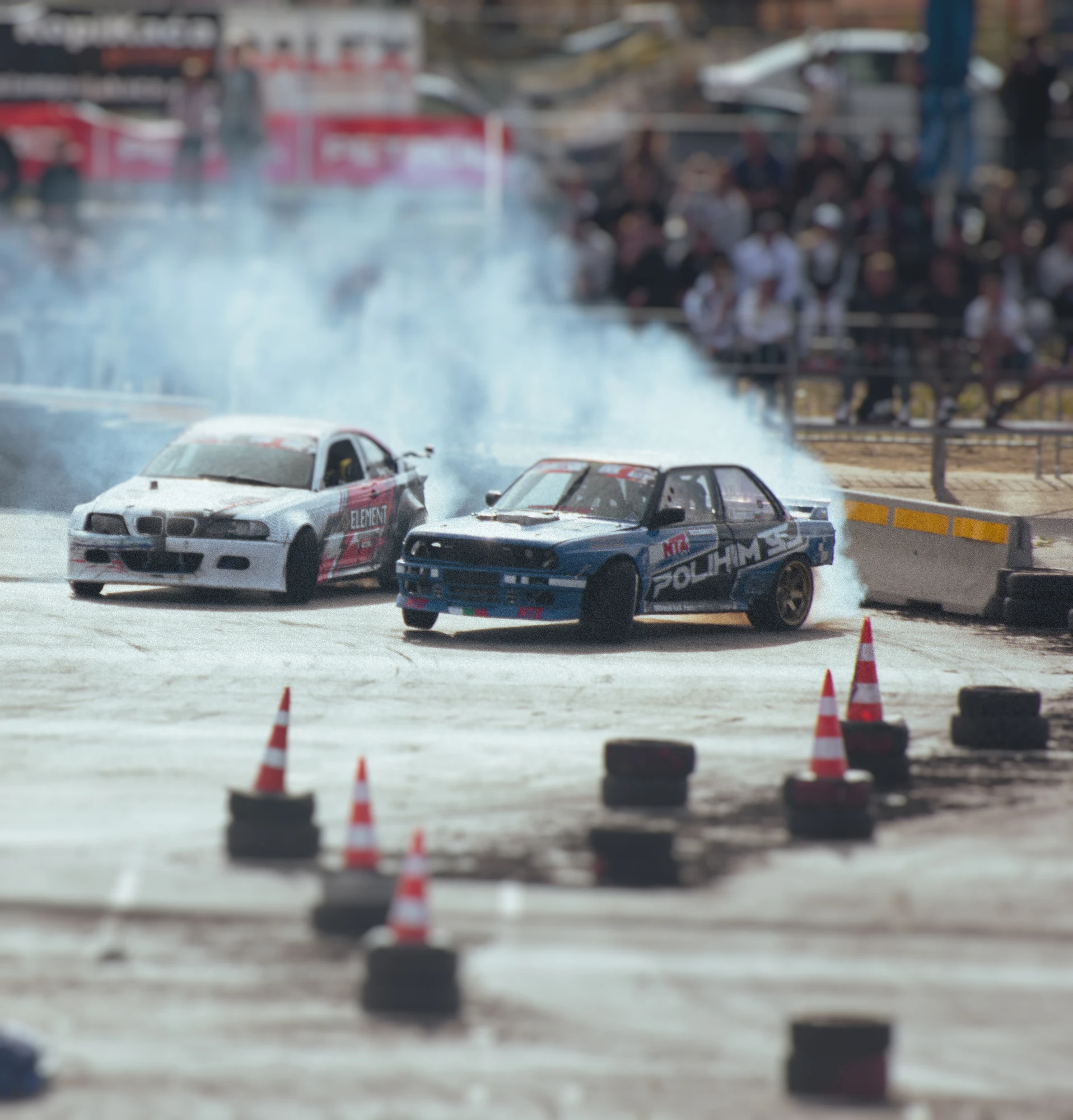 Two cars racing around a track with smoking tyres