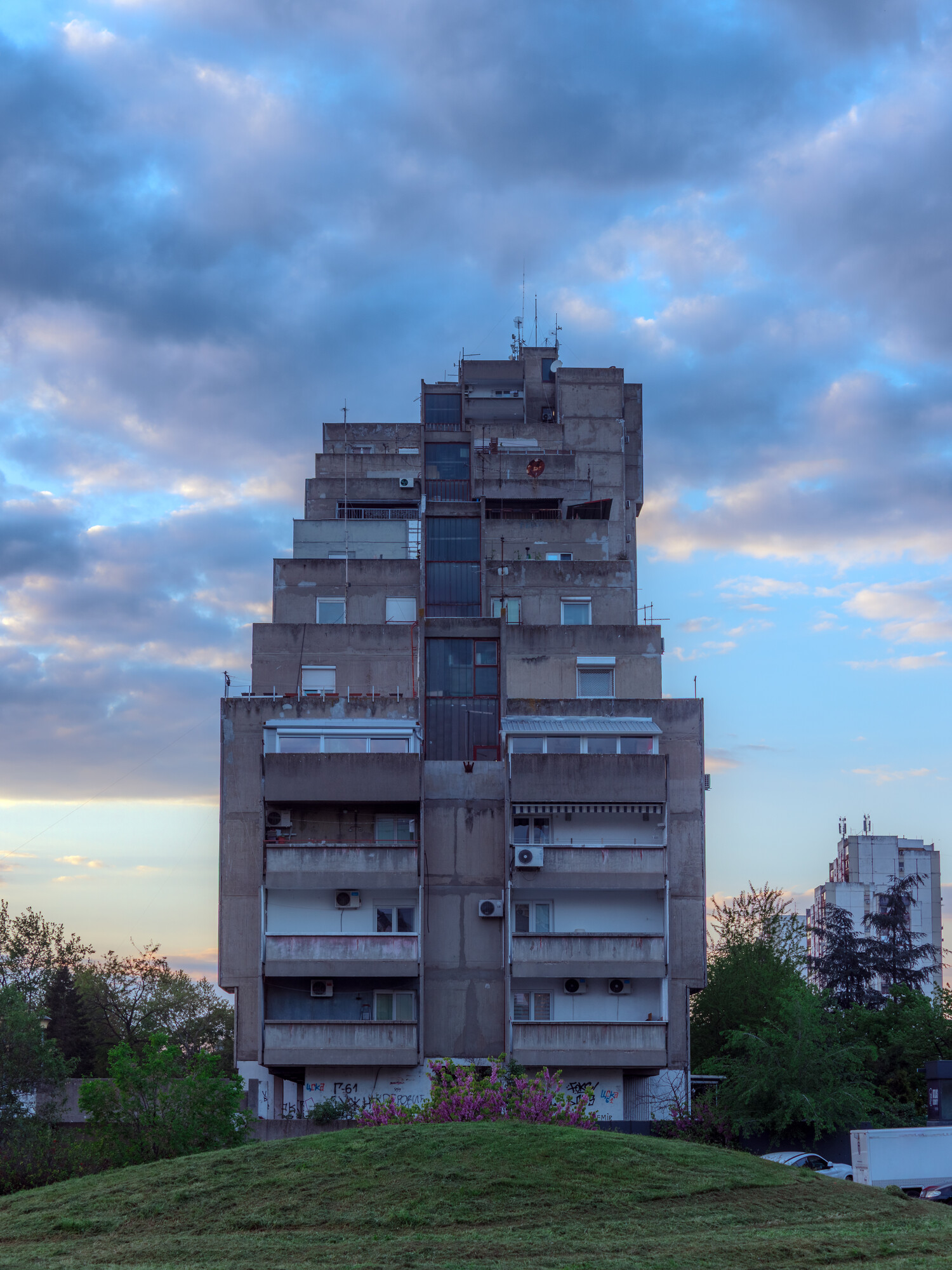 Stairs-like concrete skyscraper above a grass hill at dusk