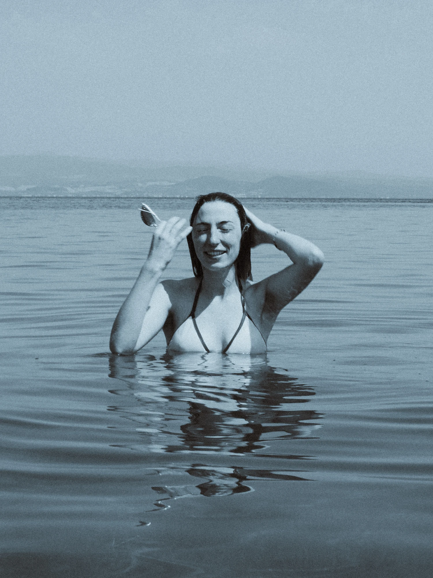 A woman standing in the sea, her reflection shuttered by the gentle waves