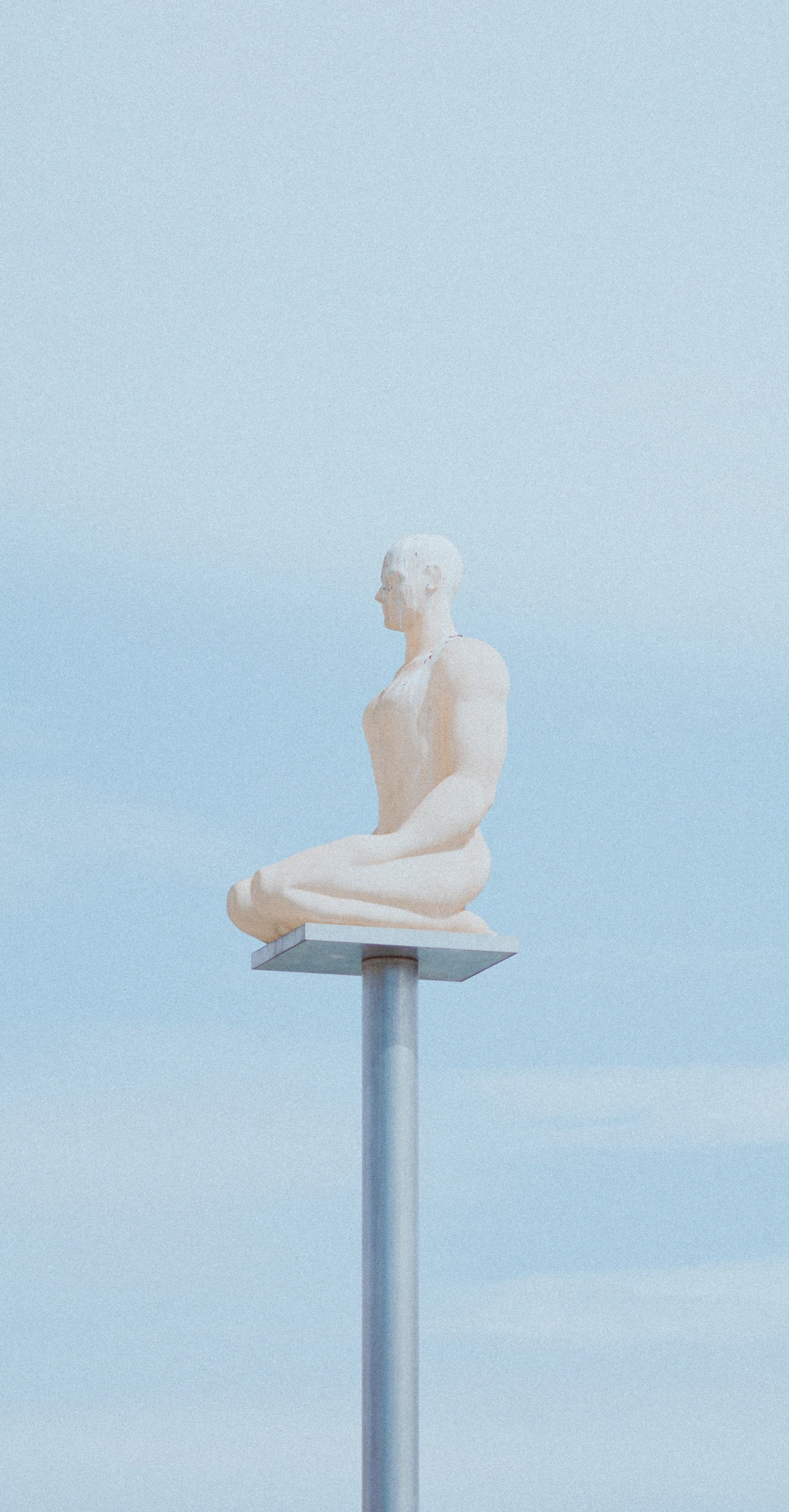 A statue of a man sitting on a pole
