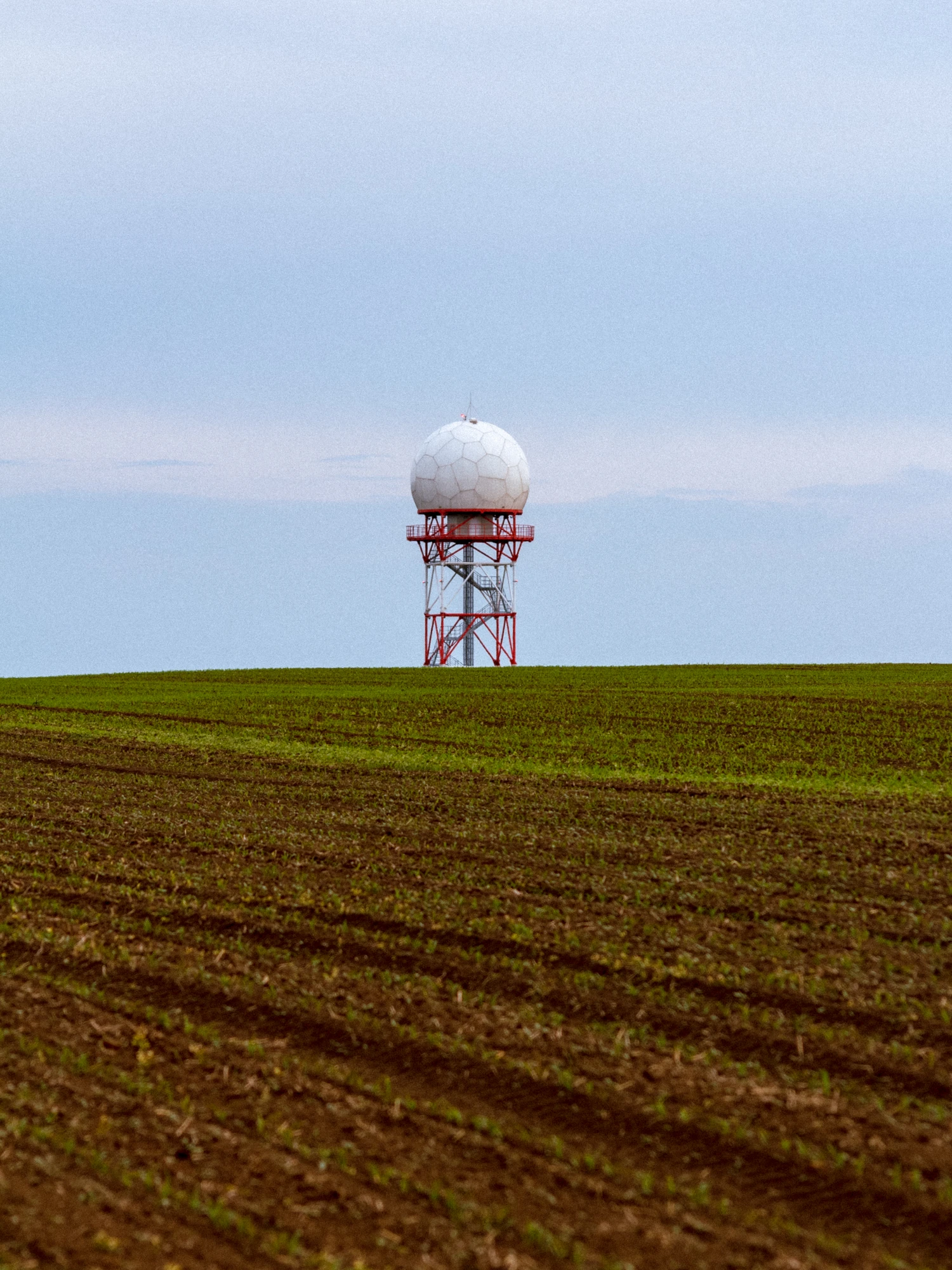 A radar tower standing in a distance over a grassy field