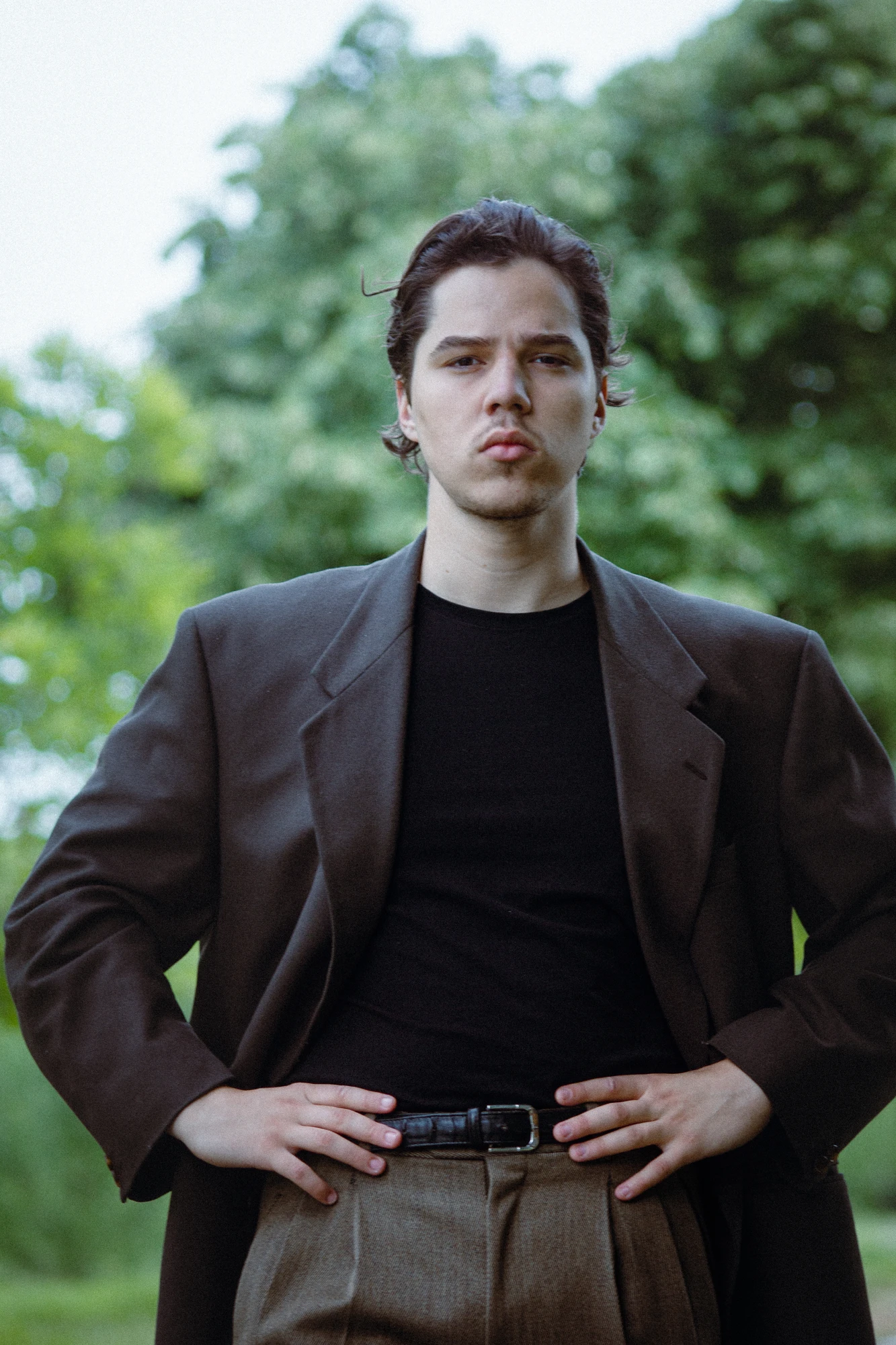 A man standing in a park with his hands on his hips