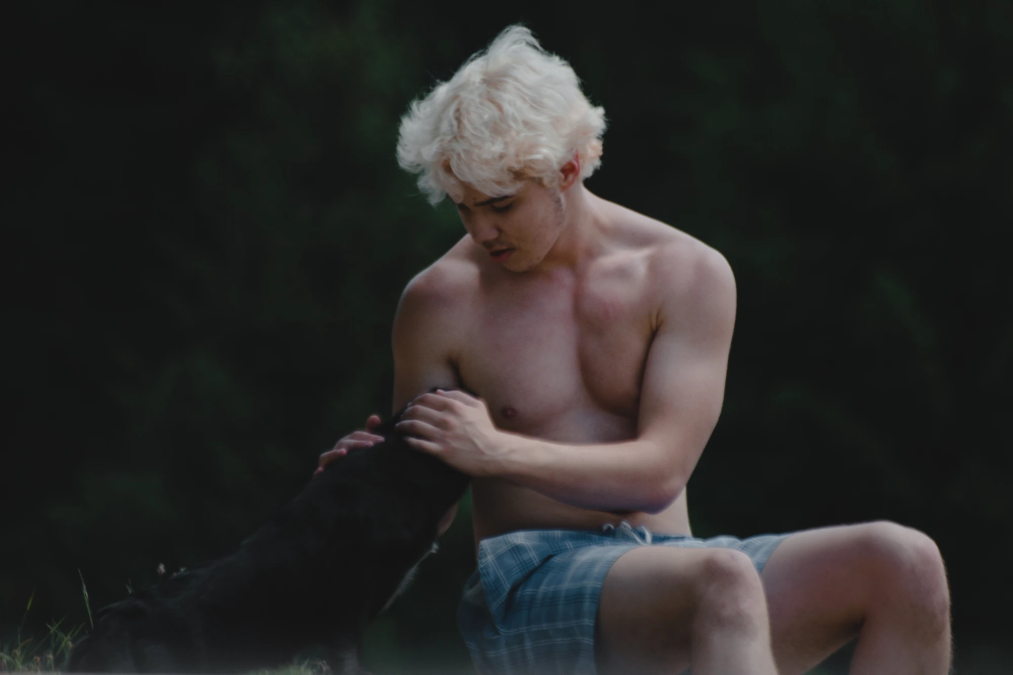 A shirtless blonde-haired young man petting a dog
