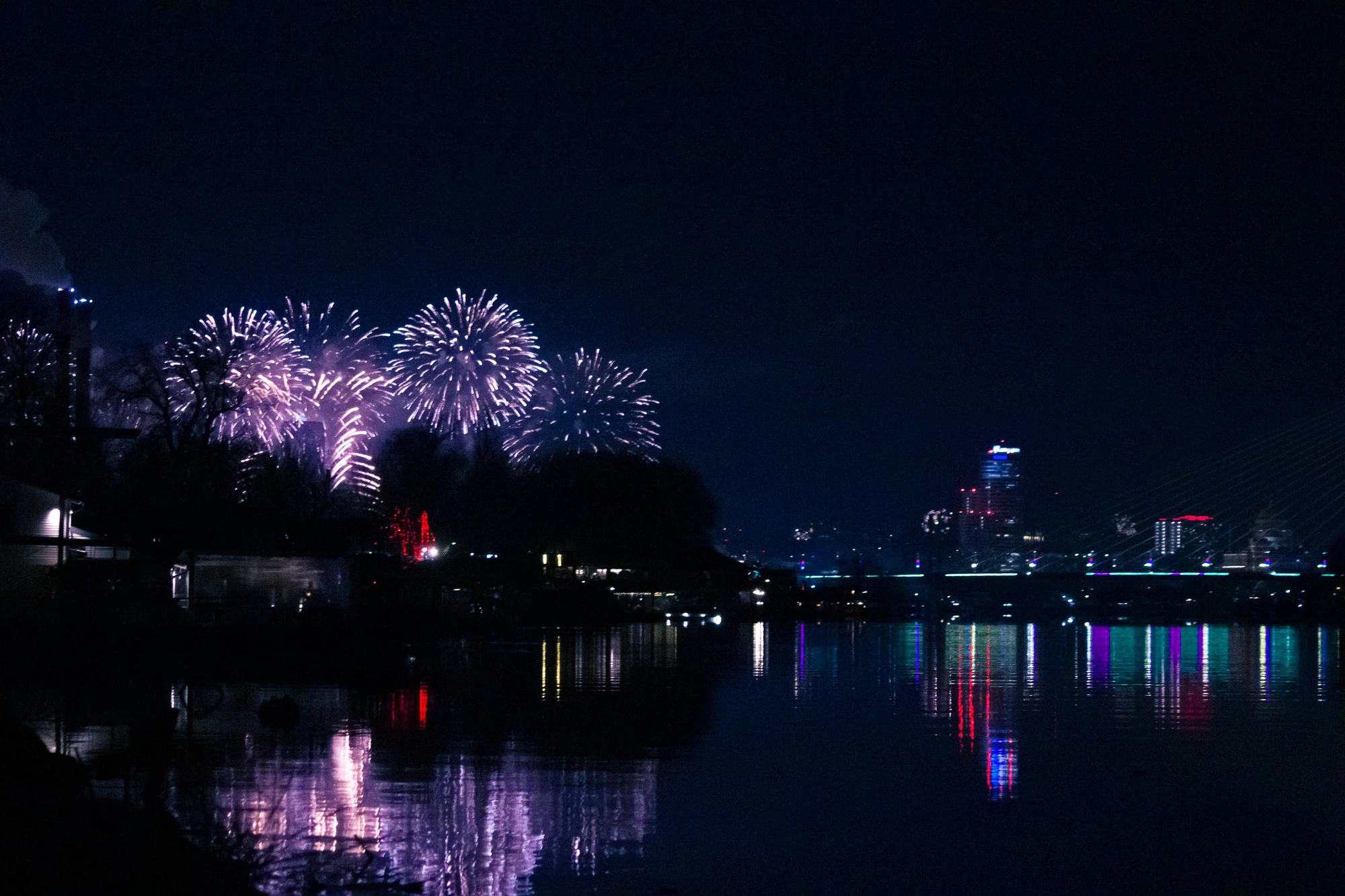 Fireworks lit up in the sky over a city on a river